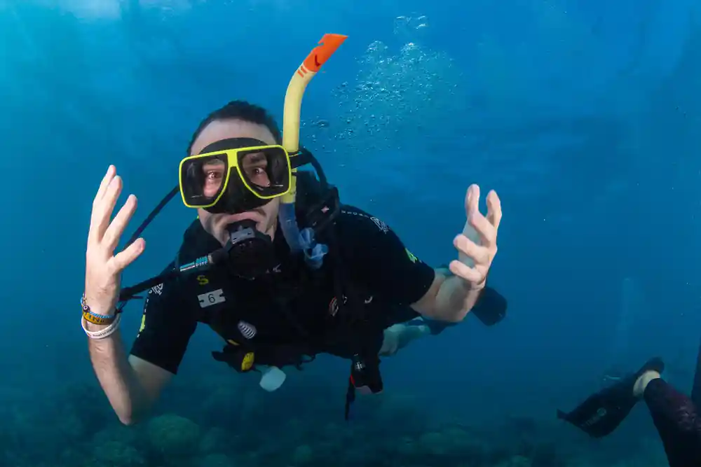 A diver reaching out towards the camera above the reef
