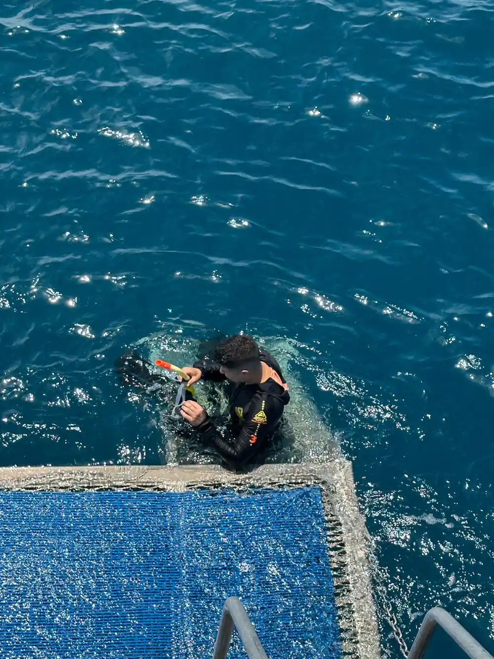 A diver sitting on the blue dive platform pulling on fins