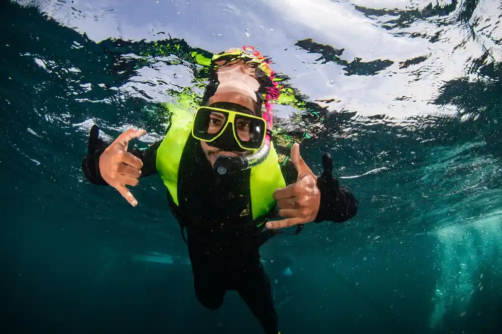 A snorkeller in a yellow vest making shaka signs at the surface