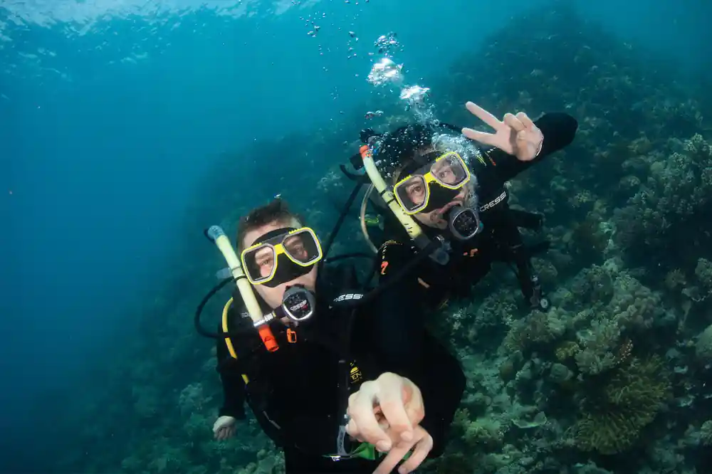 Two divers close to the lens making a peace sign underwater